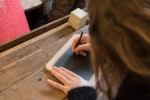 Pige skriver med griffel på lille tavle i "Den Gamle Skolestue"